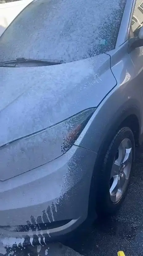 Josue spraying thick foam on a silver car in a customer's driveway